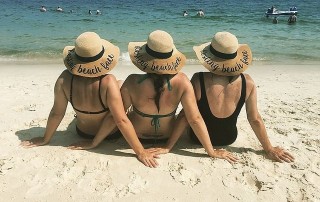 Three women sitting on beach with straw hats
