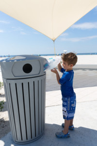 child putting items in recycling bin at the beach